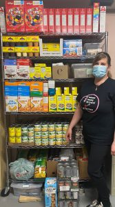 The Executive Director of Marjorie House stands in front of a fully stocked pantry shelf that spans from floor to ceiling.