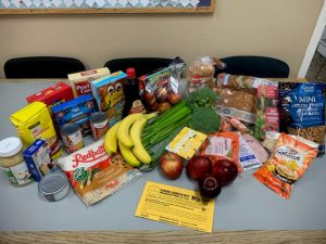 Example of a food kit from Our Kids Count, depicting fresh vegetables and groceries spread out on a large table.